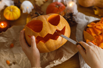 Happy Halloween! Carving halloween pumpkin. Woman holding pumpkin and knife on table with ghosts and spiders. Making halloween decorations