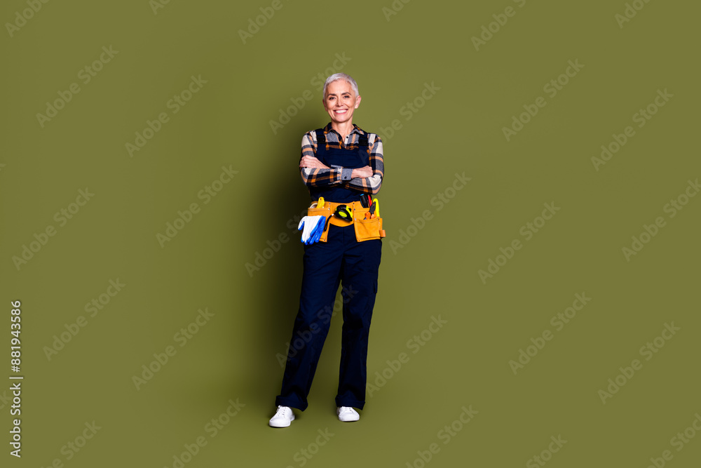 Full size photo of senior female professional expert handyman folded hands wear blue workwear overall isolated on khaki color background Full size photo of senior female professional expert handyman folded hands wear blue workwear overall isolated on khaki color background