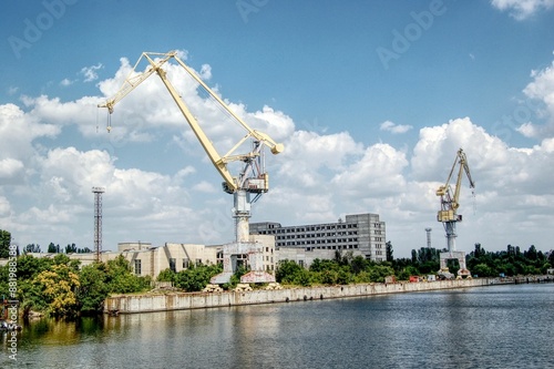 фотографія Industrial cranes and buildings along a river under a partly cloudy sky