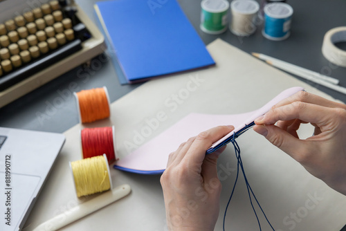 High-quality image of a person binding a book using traditional coptic stitch technique. DIY bookbinding, handcrafting, artisan book, handmade, coptic stitch, binding tools, creative, detailed process photo