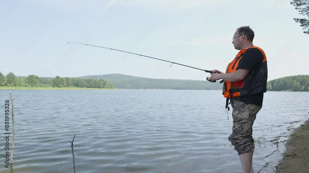 Male fisherman is standing on the riverbank with a fishing rod in his hands and catching fish. Calm outdoor recreation Male fisherman is standing on the riverbank with a fishing rod in his hands and catching fish. Calm outdoor recreation