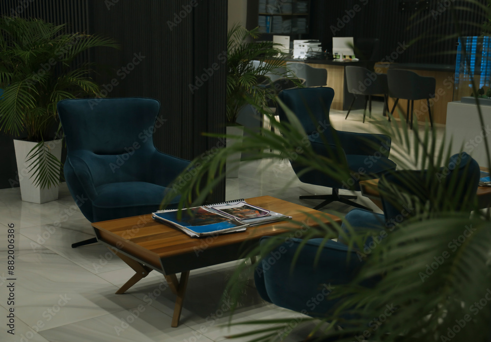 computer on a desk in a modern real estate office. Office in a loft style with black wall. workplaces with magazines on wooden tables armchairs, printers computers, plants palm trees in white pots.