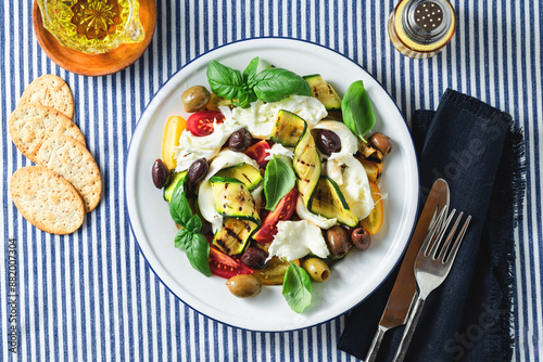 Mediterranean salad with mozzarella, olives, basil and grilled vegetables on a blue striped linen tablecloth