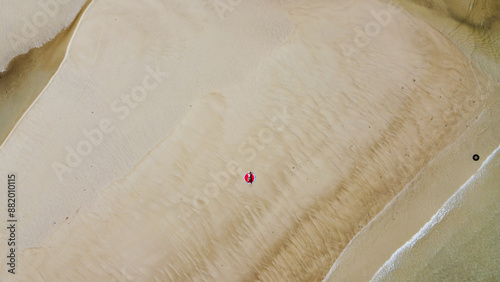 Woman wearing sun hat at the beach and lying on a white sand, Top view from flying drone.
