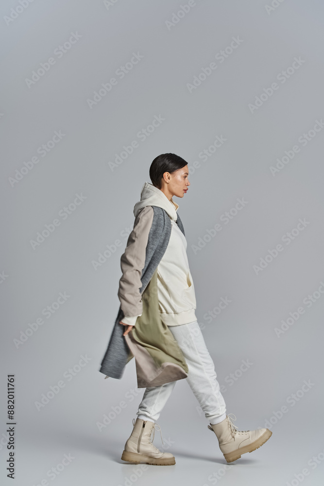 A young stylish woman walks confidently wearing a trench coat in a studio with a grey background. A young stylish woman walks confidently wearing a trench coat in a studio with a grey background.