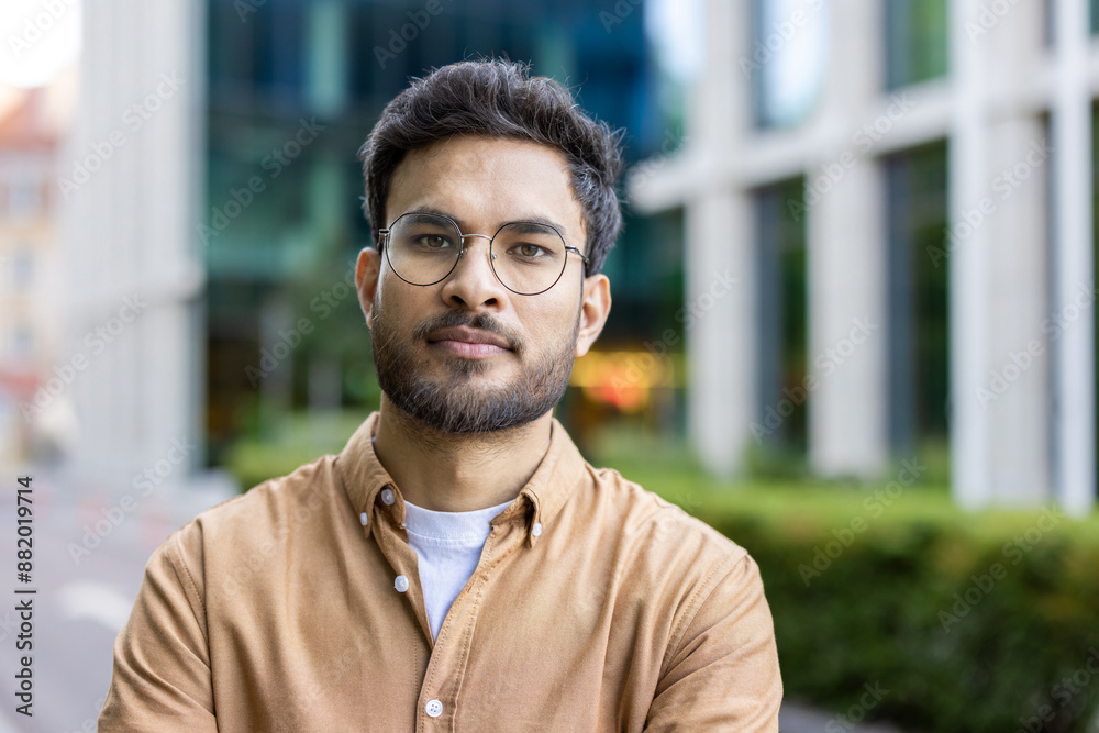 Young man with glasses and beard standing confidently outdoors in urban environment. Casual clothing and modern background highlight contemporary city life and professional attitude. Young man with glasses and beard standing confidently outdoors in urban environment. Casual clothing and modern background highlight contemporary city life and professional attitude.