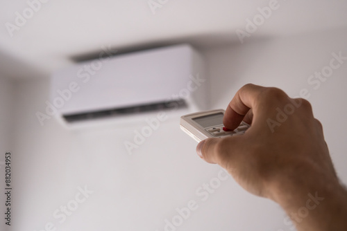 Close-up of a man's hand holding the remote control from the air conditioner that hangs on a white wall in the apartment. High quality photo