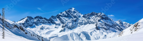 Panoramic view of majestic snow-capped mountain range under clear blue sky, showcasing beautiful winter scenery and pristine snowy peaks.