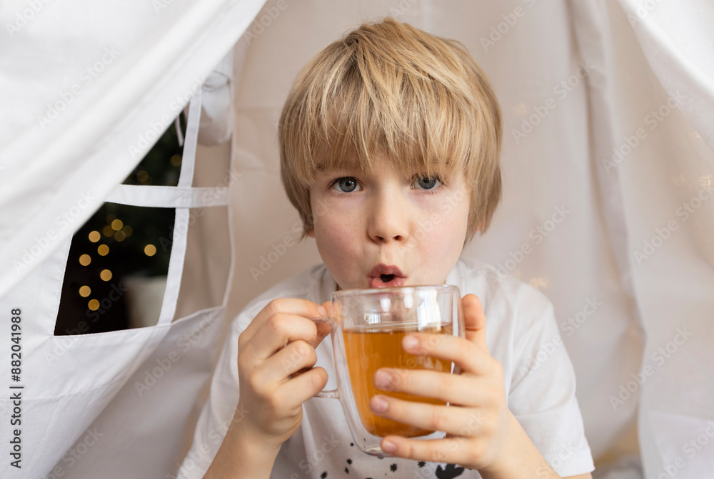 close-up of a child holding a glass mug with a hot drink of tea. A cozy home on winter weekends and holidays. Life style close-up of a child holding a glass mug with a hot drink of tea. A cozy home on winter weekends and holidays. Life style