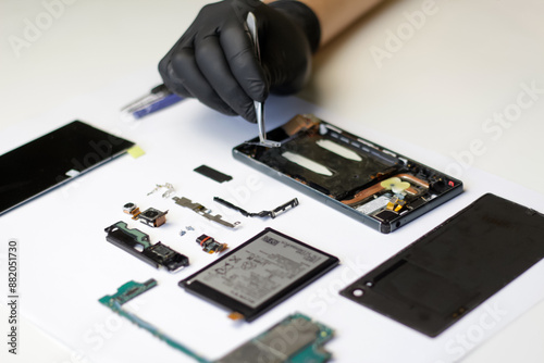 Professional repair of a disassembled smartphone, master with tweezers and gloves working on broken parts. Disassembled smartphone with parts laid out