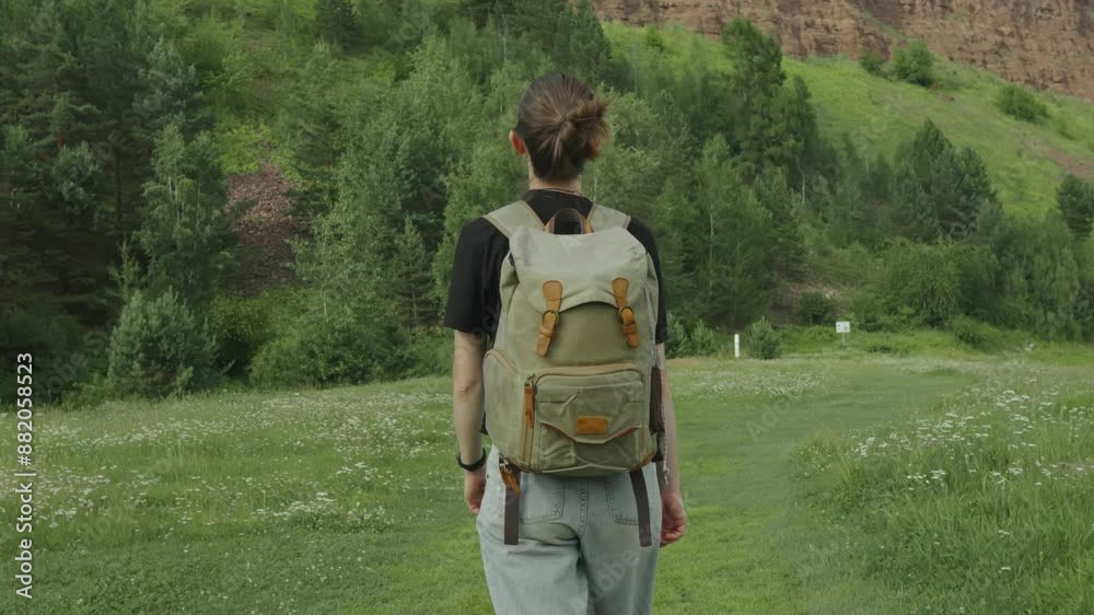 A female tourist with a backpack walks through the forest among the trees. Active trekking and unity with nature on a sunny summer day