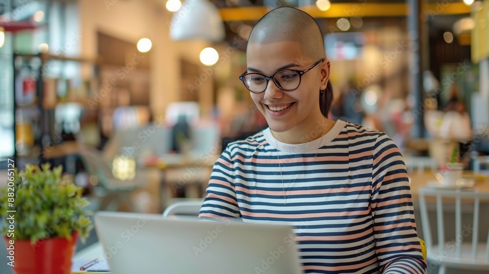 A woman with a shaved head is sitting at a table with a laptop in front of her