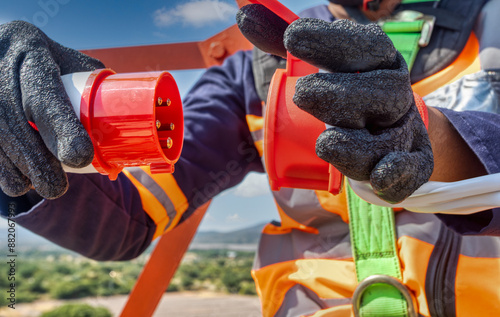 Aerial view electrician high up on the tower, high voltage plug in hand. Connecting a 380 volt high voltage, three phase plug