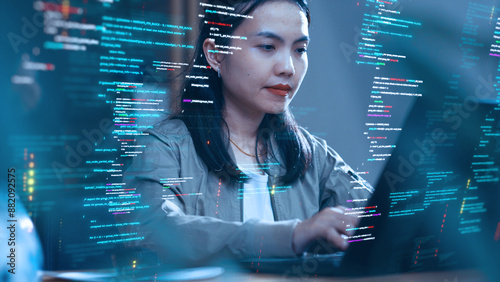 An Asian woman works with a laptop, surrounded by abstract holographic code. Concepts of software development and coding.