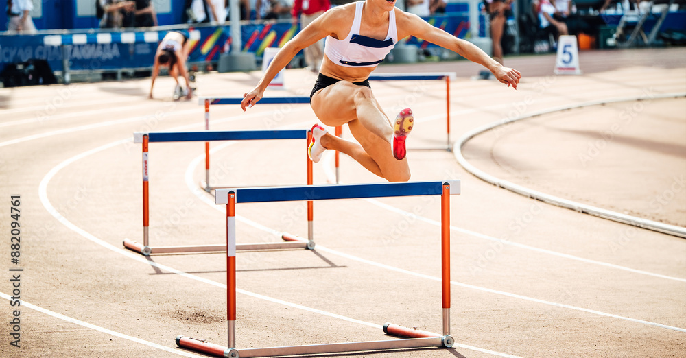 Naklejka premium female runner running 400 meters hurdles race in summer athletics championships