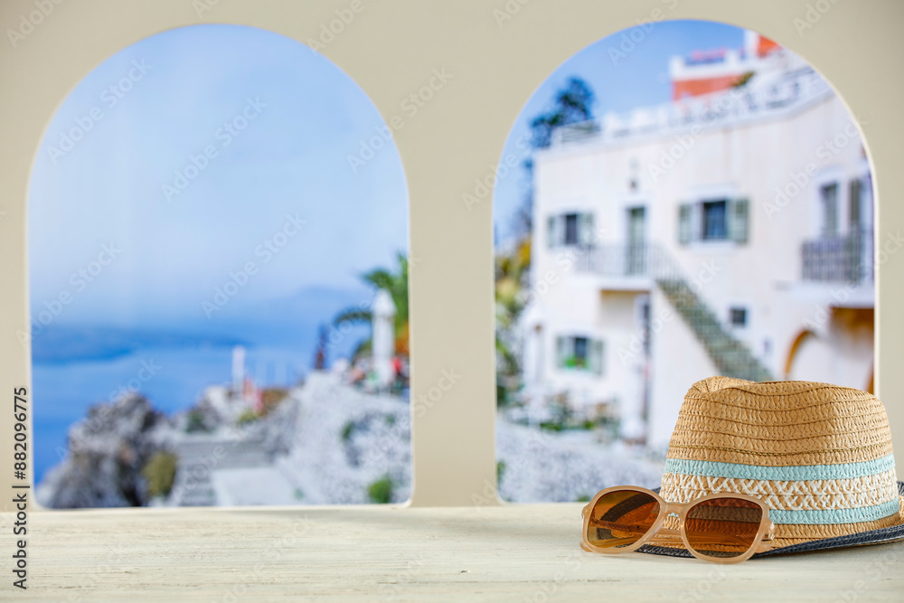 Obraz premium Towels and straw summer hat on wooden table top with copy space for products. Arched windows and blurred buildings of summer resort background.