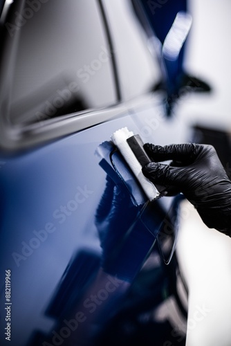 Obraz na płótnie Image shows a person applying a ceramic coating to the surface of a blue car. The person is wearing black gloves, and the setting appears to be a well-lit workshop or garage w salonie