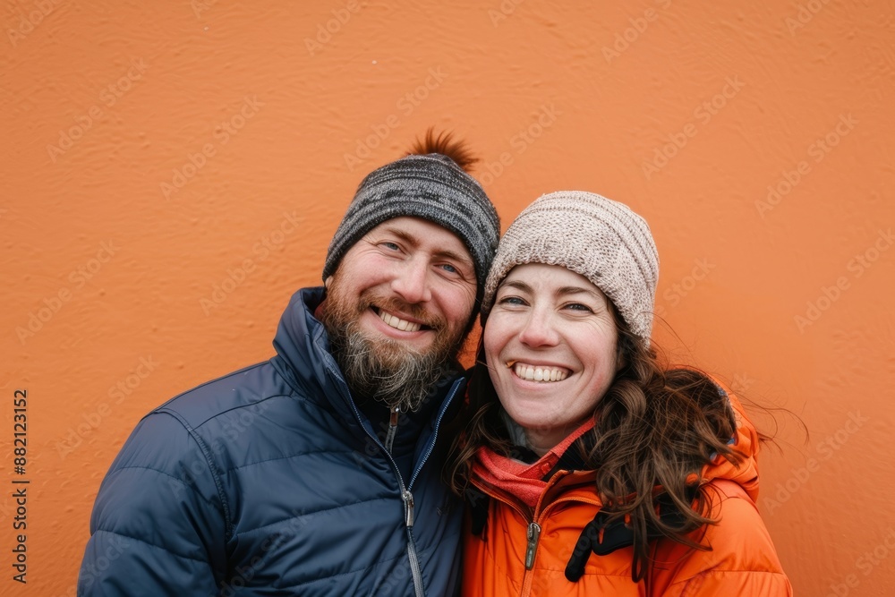 Portrait of a grinning couple in their 30s dressed in a water-resistant gilet in pastel orange background Portrait of a grinning couple in their 30s dressed in a water-resistant gilet in pastel orange background