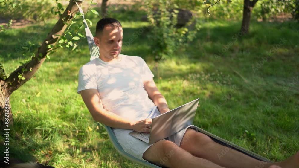 a man works on a laptop in a hammock in the garden, next to his pet dog a man works on a laptop in a hammock in the garden, next to his pet dog