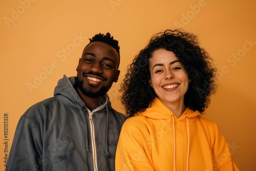 Portrait of a satisfied multiethnic couple in their 30s wearing a zip-up fleece hoodie while standing against soft orange background