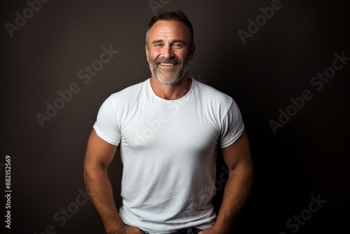 Portrait of a smiling man in his 50s dressed in a casual t-shirt while standing against bare monochromatic room