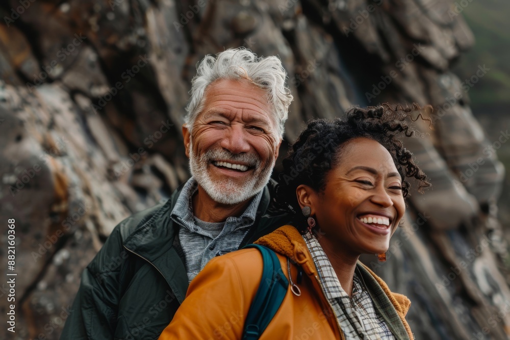Portrait of a joyful multiethnic couple in their 50s wearing a trendy bomber jacket isolated in rocky cliff background Portrait of a joyful multiethnic couple in their 50s wearing a trendy bomber jacket isolated in rocky cliff background