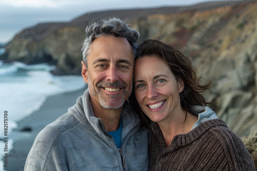 Portrait of a content couple in their 40s wearing a thermal fleece pullover on dramatic coastal cliff background Portrait of a content couple in their 40s wearing a thermal fleece pullover on dramatic coastal cliff background