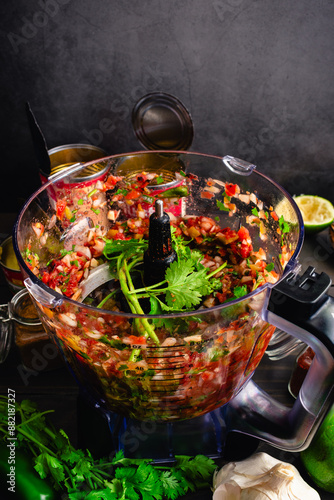 Chunky Salsa in a Food Processor with Unblended Cilantro Sprigs: Freshly made blender salsa in a food processor bowl surrounded by ingredients photo