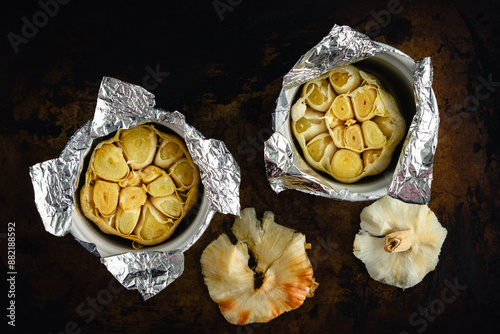 Roasted Garlic Bulbs in Ramekins Covered with Foil: Two heads of garlic that have been roasted in olive oil inside small ceramic bowls photo