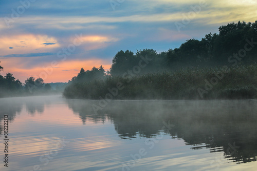 At sunset in summer, the river and forest are shrouded in fog.