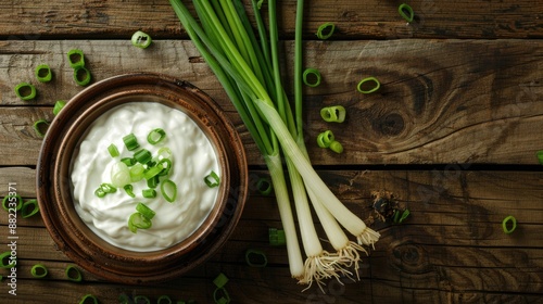 Bowl of sour cream and green onion on wooden table viewed from above