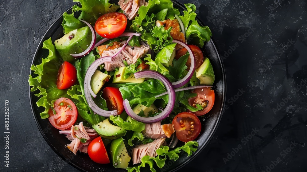 A salad with lettuce, tomatoes, cucumber, onion, avocado, and tomatoes on a black plate A salad with lettuce, tomatoes, cucumber, onion, avocado, and tomatoes on a black plate