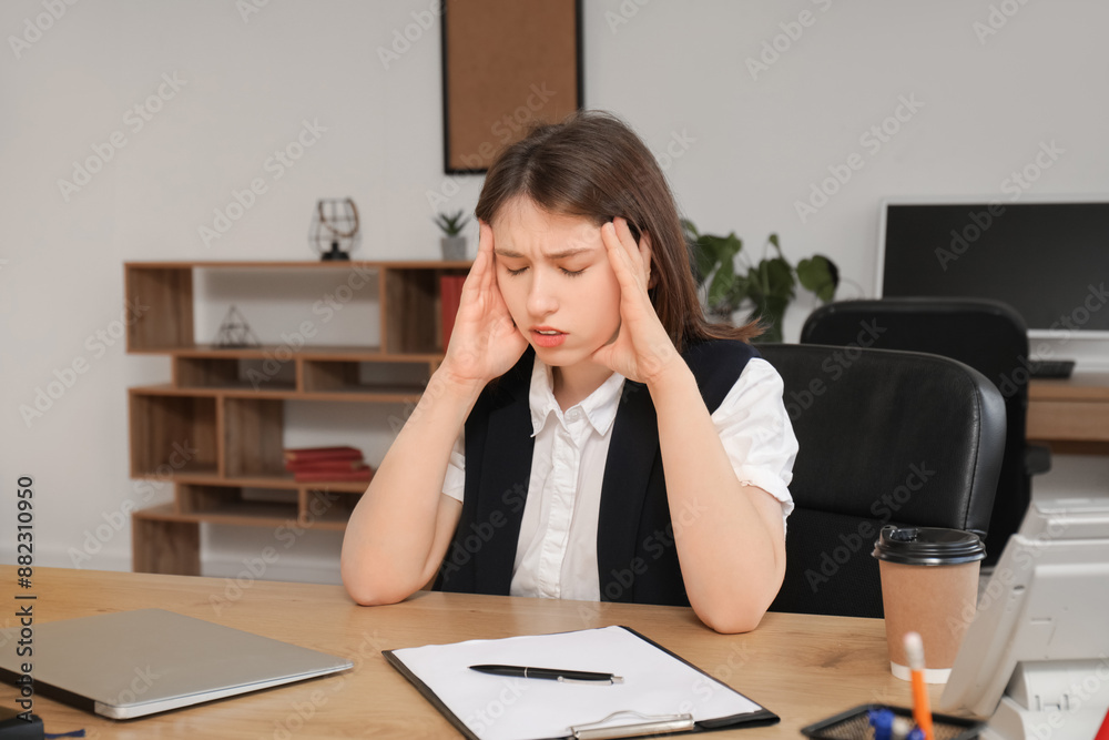 Pretty businesswoman suffering from headache at table in modern office Pretty businesswoman suffering from headache at table in modern office