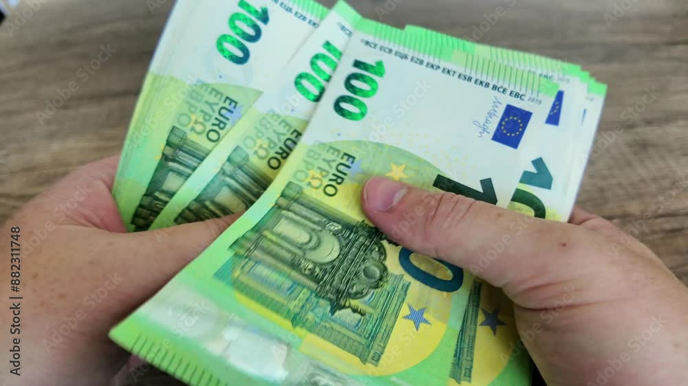 Person counts out 100 euro banknotes and places them one by one on a office desk