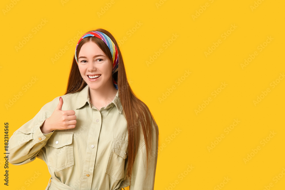 Fototapeta premium Success and approval concept, happy young woman showing thumbs up gesture with positive attitude and smiling expression on a bright yellow background