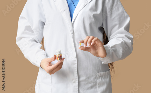 Young female doctor with pills on beige background