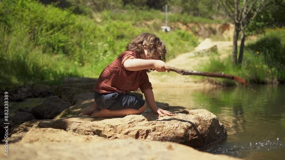 A young boy is playing in a river with a stick. The boy is sitting on a rock and is holding a stick in his hand. The water is calm and the boy is focused on the water
A young boy is playing in a river with a stick. The boy is sitting on a rock and is holding a stick in his hand. The water is calm and the boy is focused on the water