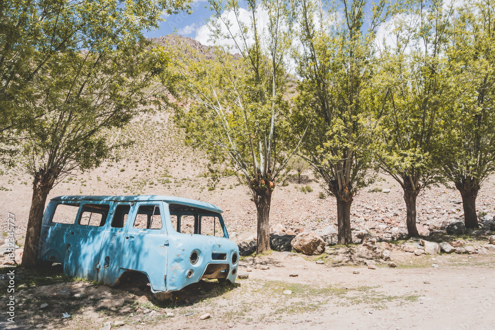 Old car died in Tajikistan mountains in Pamir, rotten rusty blue car body, soviet legacy of the auto industry