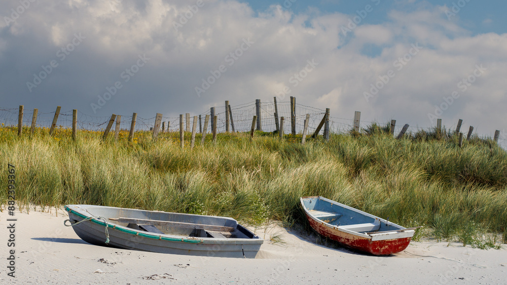 Two old fishing boats on the beach next to sand grass