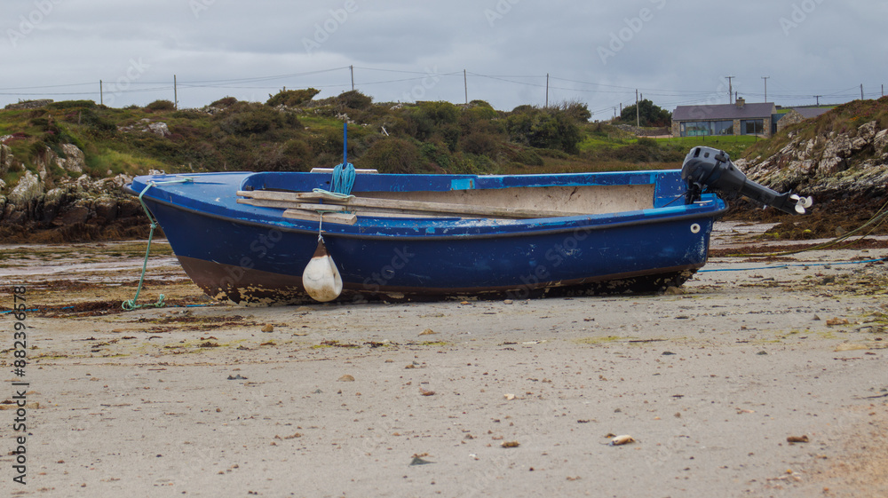 Blue fishing boat on the beach waiting for the tide to come in and the coastline in the background.