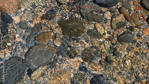 Background of shiny pebbles on the river bottom. Abstract pattern of pebbles under the surface of the water.