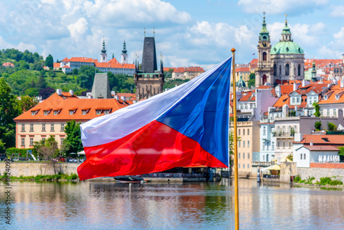 Photography A vibrant Czech flag flutters in the foreground with a panoramic view of Prague historic architecture and the Vltava River under a clear sky