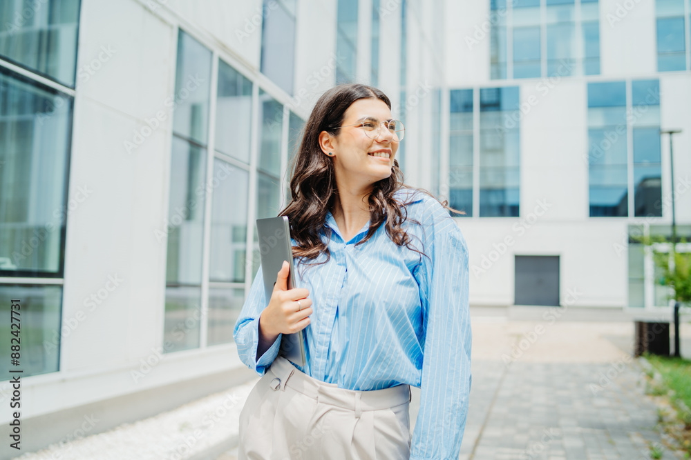 One beautiful young successful business woman going to work at business office modern building while holding laptop and wearing glasses One beautiful young successful business woman going to work at business office modern building while holding laptop and wearing glasses