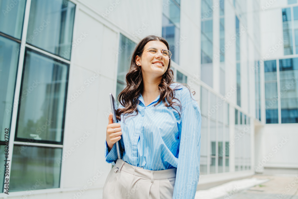 One beautiful young successful business woman going to work at business office modern building while holding laptop and wearing glasses One beautiful young successful business woman going to work at business office modern building while holding laptop and wearing glasses
