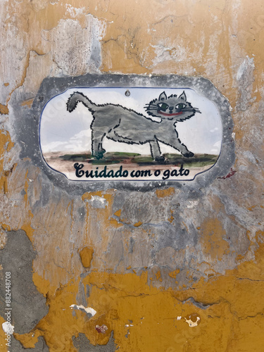 Foto A rustic ceramic sign reading Cuidado com o gato features a painted cat on a weathered ochre wall in bright daylight, ideal for Portuguese travel and pet warning concepts