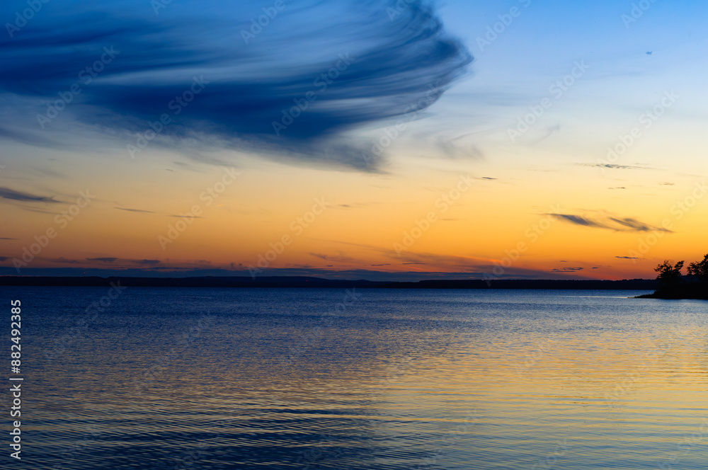 As dusk falls over the St. Lawrence River near Montreal, the horizon is alight with vibrant hues of orange and blue, while swirling clouds above mirror their vivid dance on the serene river's surface As dusk falls over the St. Lawrence River near Montreal, the horizon is alight with vibrant hues of orange and blue, while swirling clouds above mirror their vivid dance on the serene river's surface