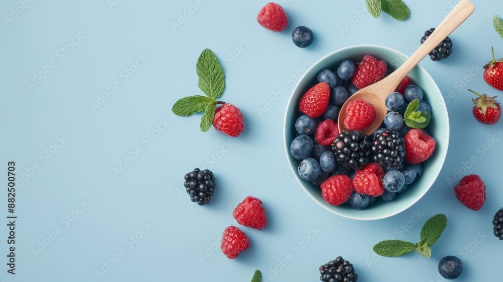A flat lay featuring a bowl of mixed berries, a wooden spoon, and a few scattered mint leaves on a light blue background A flat lay featuring a bowl of mixed berries, a wooden spoon, and a few scattered mint leaves on a light blue background
