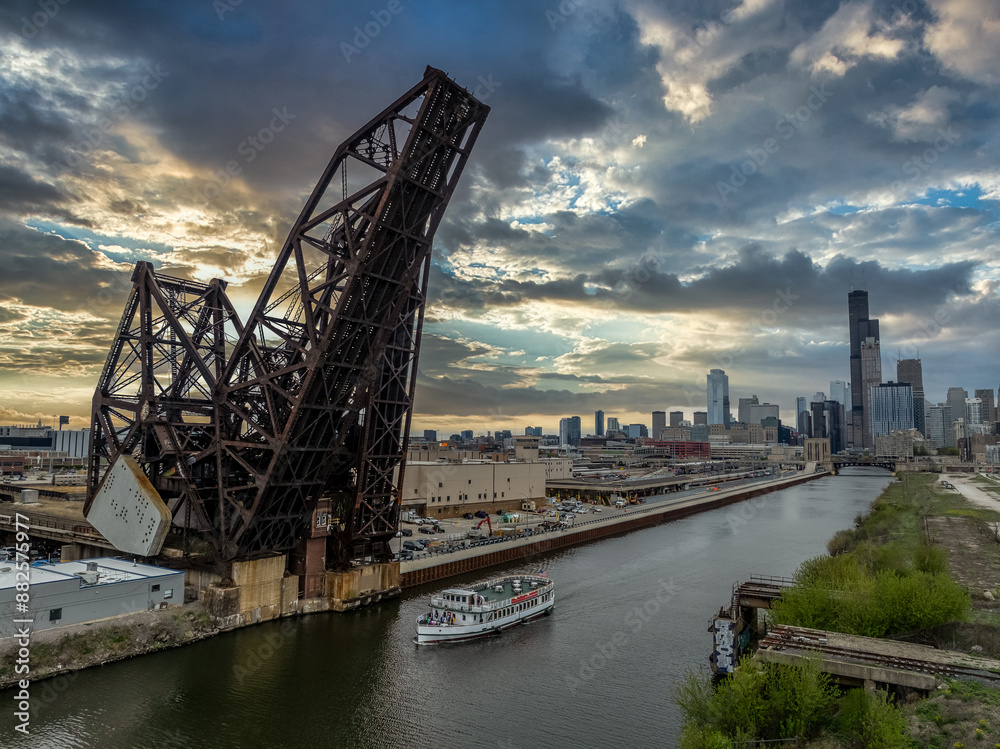 River boat passes under the St. Charles Air Line Bridge, steel railroad drawbridge over the Chicago river with dramatic sunset sky