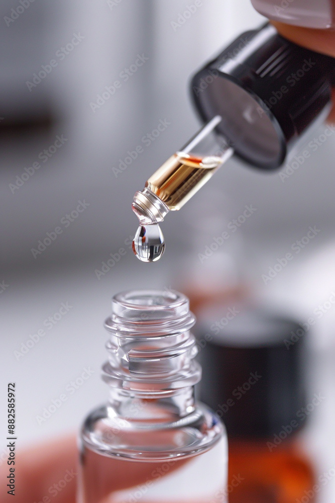 Close-up of a dropper dispensing a single drop of clear liquid into a glass bottle, with a clean, minimalistic background. Close-up of a dropper dispensing a single drop of clear liquid into a glass bottle, with a clean, minimalistic background.
