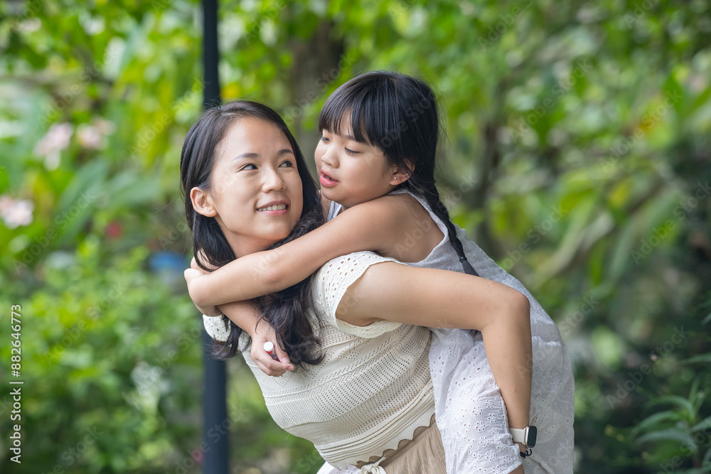 A twenty-something Chinese Malaysian woman and a six-year-old girl spending time together among the greenery and flowers at a stylish cafe in Selangor, Malaysia, on a sunny early summer afternoon.